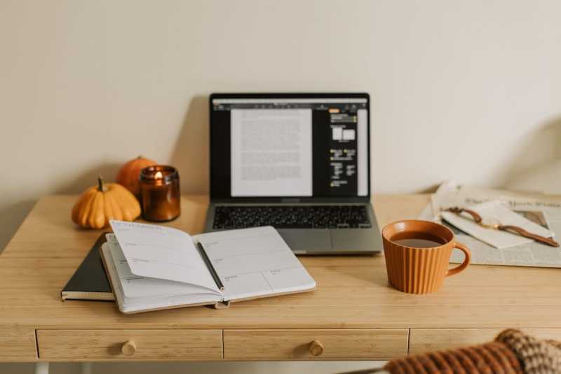 A photograph of a notebook, laptop, and cup of coffee